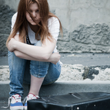 A sad teen girl with long hair sits alone with a suitcase